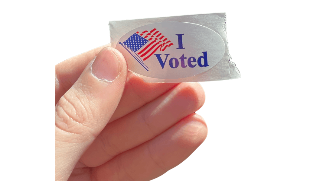 Close-up of a hand holding an “I Voted” sticker with a U.S. flag, symbolizing civic engagement and voter turnout in the 2024 U.S. election—highlighting the overlooked voters targeted by strategic campaigns in the article “The Hidden Strategy of 2024: How Campaigns Compel America’s Overlooked Voters.”